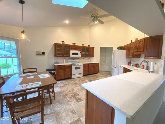 kitchen featuring kitchen peninsula, vaulted ceiling with skylight, white appliances, ceiling fan, and hanging light fixtures