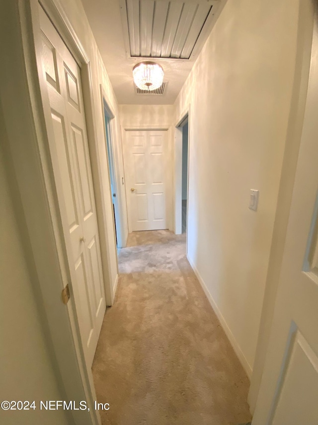 hallway featuring light colored carpet and baseboards