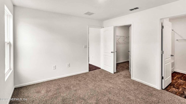 unfurnished bedroom with a walk in closet, a closet, dark carpet, and multiple windows