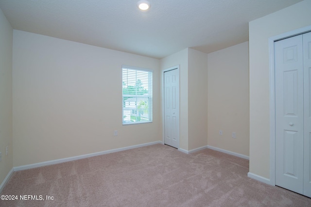 unfurnished bedroom with multiple closets and light carpet