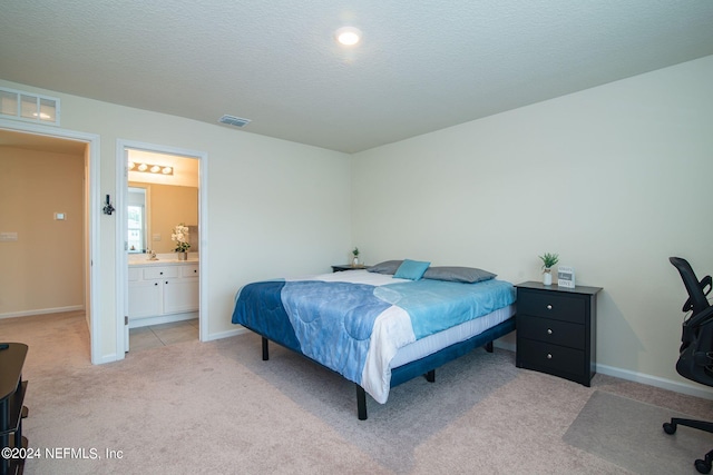 bedroom featuring ensuite bath, light carpet, and a textured ceiling