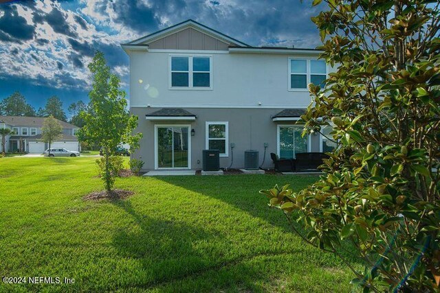 rear view of house with central AC unit and a lawn