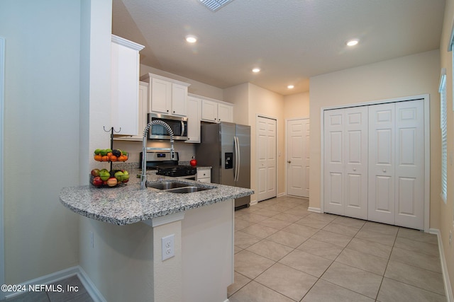 kitchen with white cabinets, light tile patterned floors, kitchen peninsula, stainless steel appliances, and light stone countertops