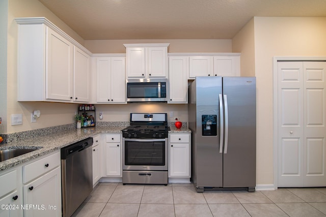 kitchen featuring appliances with stainless steel finishes, light tile patterned floors, white cabinets, and light stone counters