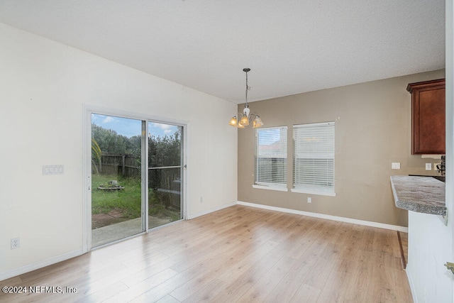 unfurnished dining area featuring light hardwood / wood-style floors, a notable chandelier, and a textured ceiling