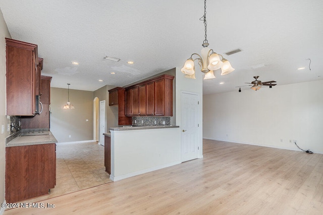 kitchen with tasteful backsplash, light hardwood / wood-style floors, ceiling fan with notable chandelier, pendant lighting, and a textured ceiling