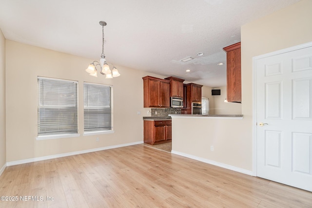 kitchen featuring a notable chandelier, stainless steel microwave, backsplash, and light wood-style floors