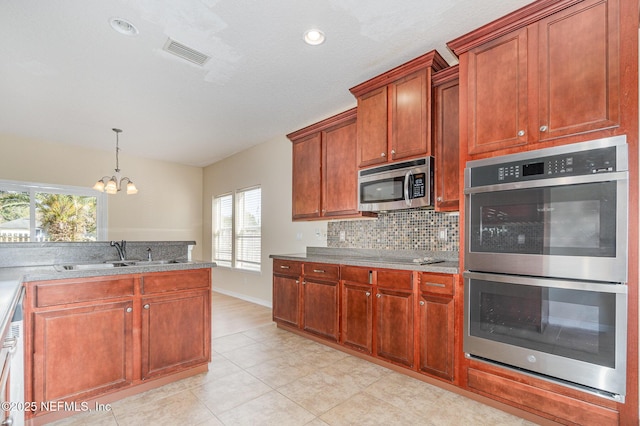 kitchen with stainless steel appliances, a sink, visible vents, hanging light fixtures, and tasteful backsplash