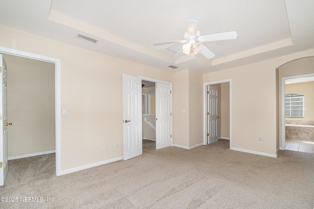 unfurnished bedroom featuring arched walkways, carpet flooring, baseboards, a spacious closet, and a tray ceiling