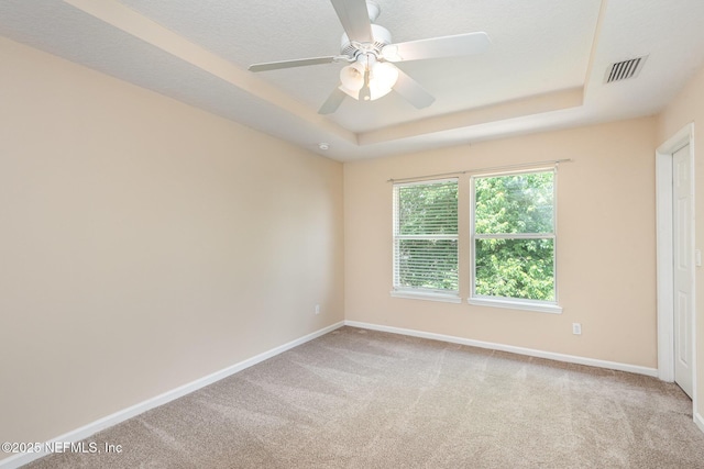 carpeted empty room with visible vents, a ceiling fan, a tray ceiling, and baseboards