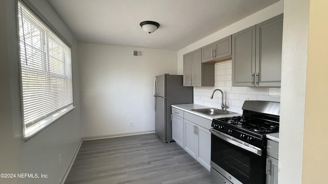 kitchen with decorative backsplash, gray cabinets, stainless steel appliances, light countertops, and a sink