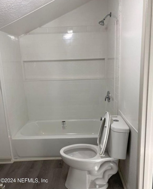 bathroom with washtub / shower combination, lofted ceiling, toilet, and wood finished floors