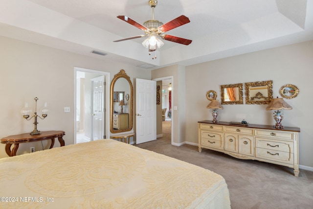 carpeted bedroom featuring ceiling fan, connected bathroom, and a tray ceiling