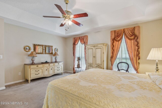 carpeted bedroom with ceiling fan and a tray ceiling