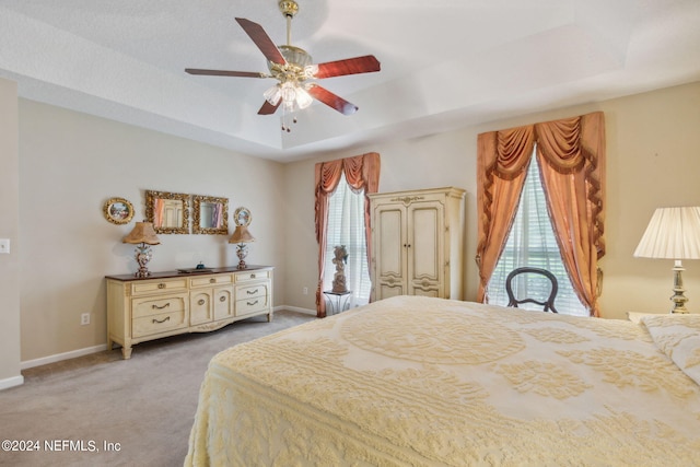 carpeted bedroom featuring multiple windows, access to exterior, a raised ceiling, and ceiling fan