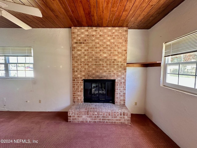 unfurnished living room featuring wood ceiling, ceiling fan, a brick fireplace, and carpet floors