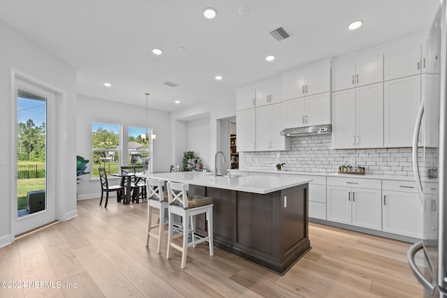 kitchen with white cabinets, pendant lighting, light hardwood / wood-style flooring, and an island with sink