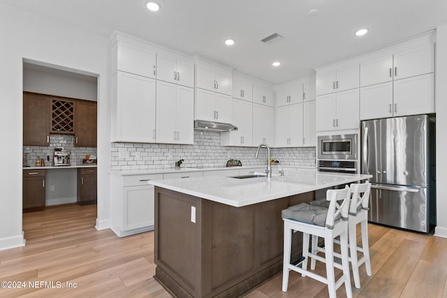 kitchen featuring stainless steel appliances, backsplash, light hardwood / wood-style flooring, and an island with sink