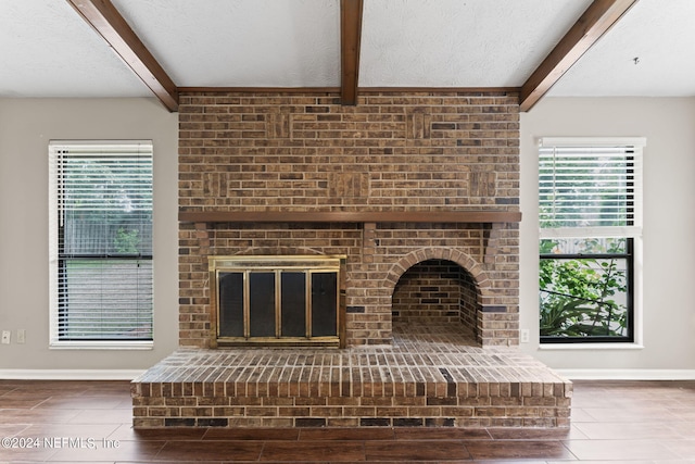 unfurnished living room with a fireplace, beam ceiling, a textured ceiling, and a healthy amount of sunlight