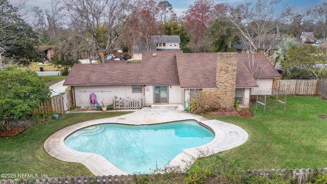 back of property with a fenced in pool and a lawn