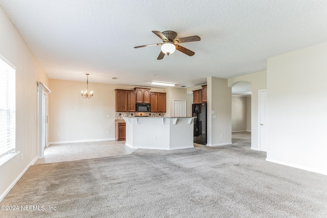 unfurnished living room featuring a textured ceiling, light carpet, and ceiling fan with notable chandelier