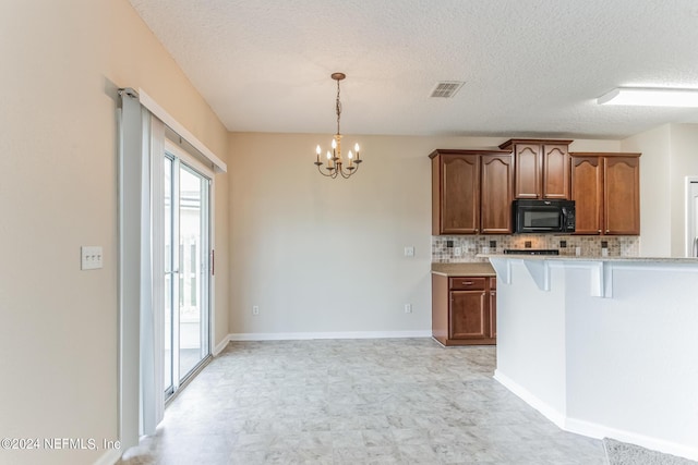 kitchen featuring decorative light fixtures, a textured ceiling, tasteful backsplash, a breakfast bar area, and a chandelier