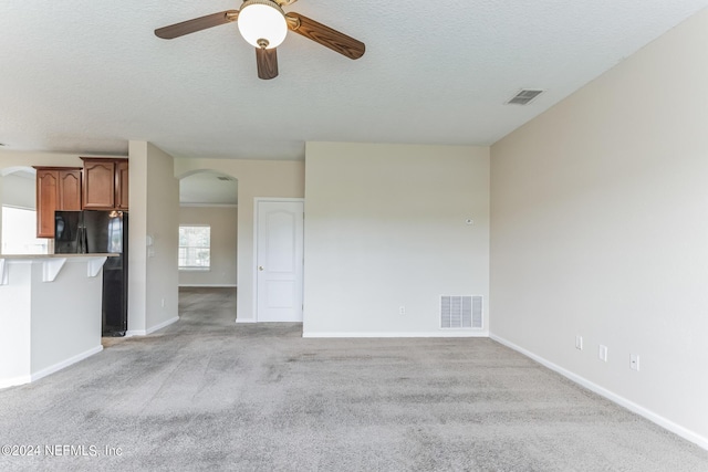 unfurnished living room featuring a textured ceiling, ceiling fan, and light colored carpet