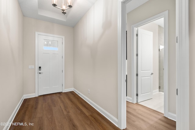 entrance foyer with a tray ceiling, baseboards, and wood finished floors