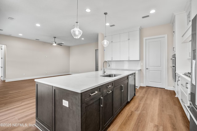 kitchen with a kitchen island with sink, a sink, stainless steel appliances, white cabinets, and light countertops