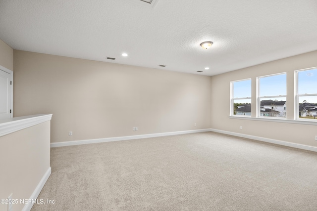 spare room with visible vents, baseboards, light colored carpet, and a textured ceiling