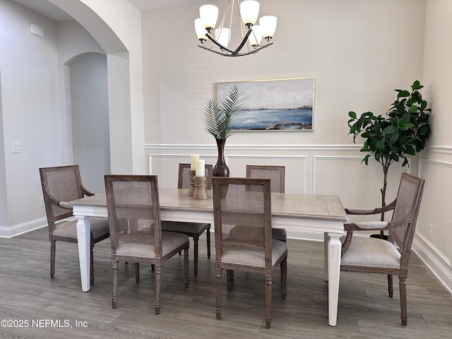 95014 Brookhill Pl, Fernandina Beach, FL 32034 - dining room featuring arched walkways, a chandelier, a decorative wall, wood finished floors, and a wainscoted wall