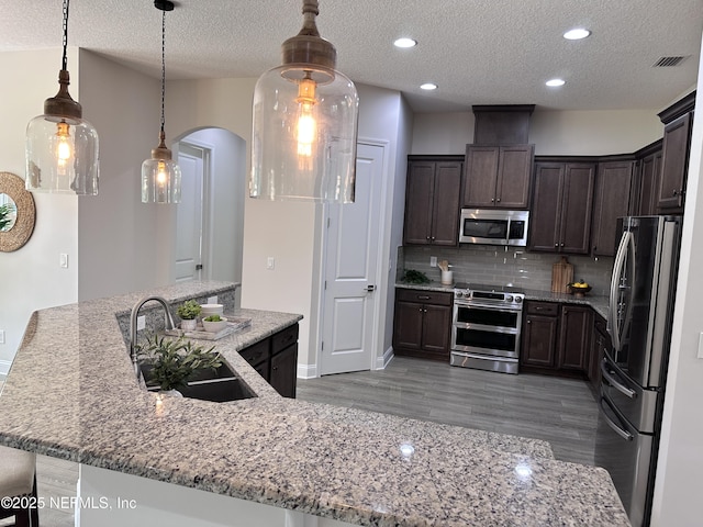 95014 Brookhill Pl, Fernandina Beach, FL 32034 - kitchen with stainless steel appliances, arched walkways, dark brown cabinets, a textured ceiling, and light wood finished floors