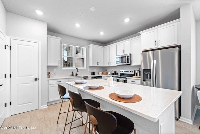 kitchen with a breakfast bar, a center island, appliances with stainless steel finishes, light hardwood / wood-style floors, and white cabinetry