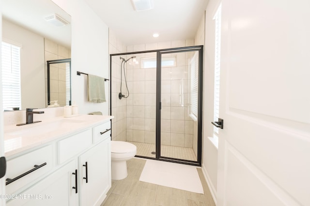 bathroom featuring a shower with door, vanity, and toilet