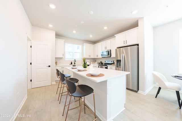 kitchen featuring white cabinetry, a center island, light hardwood / wood-style flooring, a breakfast bar, and appliances with stainless steel finishes