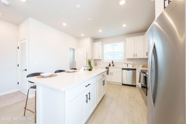 kitchen with a center island, a kitchen breakfast bar, light hardwood / wood-style flooring, white cabinets, and appliances with stainless steel finishes