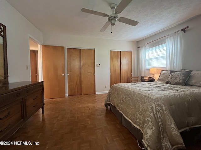 bedroom with ceiling fan, two closets, a textured ceiling, and dark parquet flooring