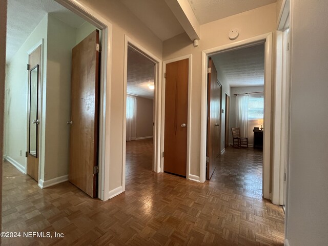 corridor featuring dark parquet floors, plenty of natural light, and a textured ceiling