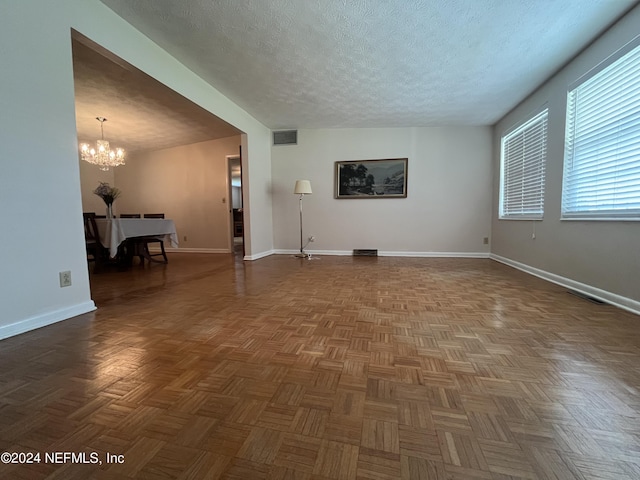 unfurnished living room featuring a textured ceiling, a notable chandelier, and dark parquet flooring