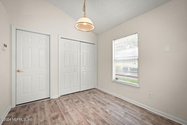 unfurnished bedroom featuring lofted ceiling, a textured ceiling, and light wood-type flooring