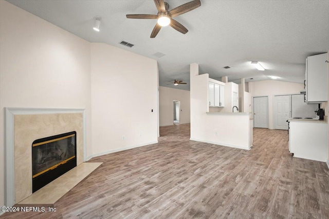 unfurnished living room with lofted ceiling, ceiling fan, a high end fireplace, a textured ceiling, and light wood-type flooring