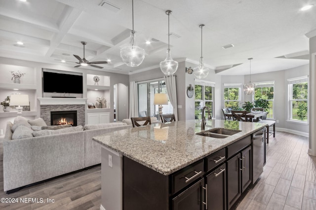 kitchen with coffered ceiling, sink, pendant lighting, a center island with sink, and a fireplace