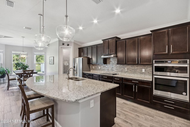 kitchen featuring backsplash, a breakfast bar, a kitchen island with sink, sink, and hanging light fixtures