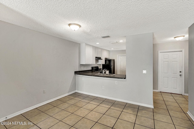 kitchen featuring white cabinets, black refrigerator, sink, a textured ceiling, and light tile patterned flooring