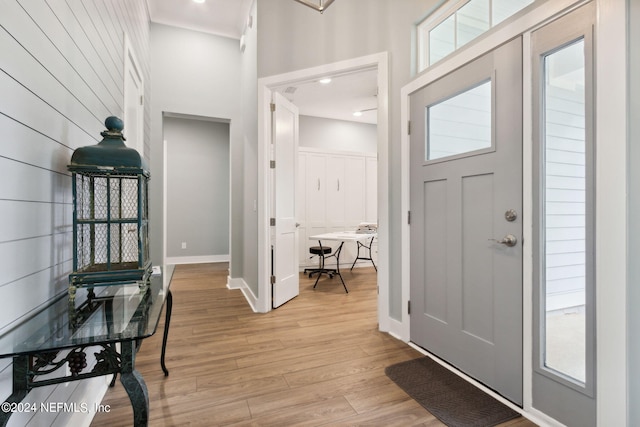 foyer with light wood-type flooring, a towering ceiling, and baseboards