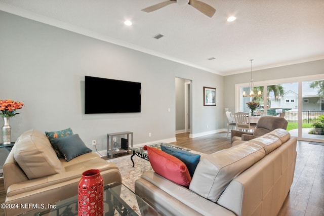 living room with visible vents, ornamental molding, wood finished floors, baseboards, and ceiling fan with notable chandelier