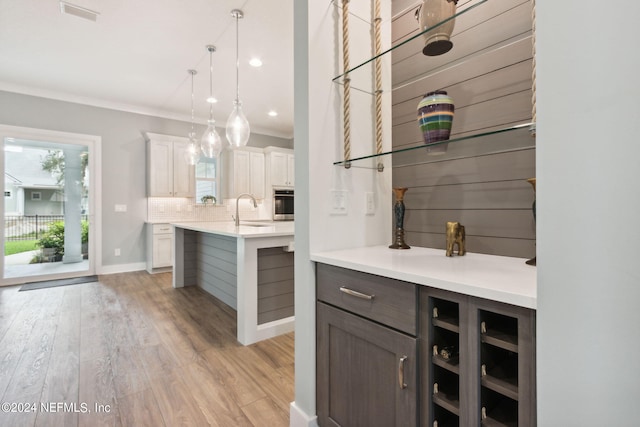 bar featuring oven, a sink, visible vents, light wood-style floors, and tasteful backsplash