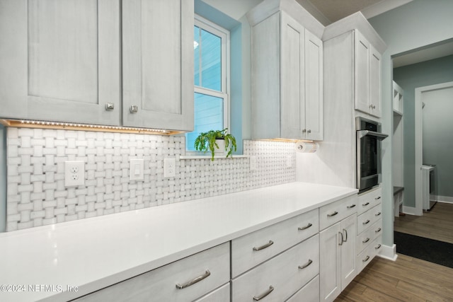 kitchen featuring dark wood-style floors, light countertops, backsplash, white cabinetry, and stainless steel oven