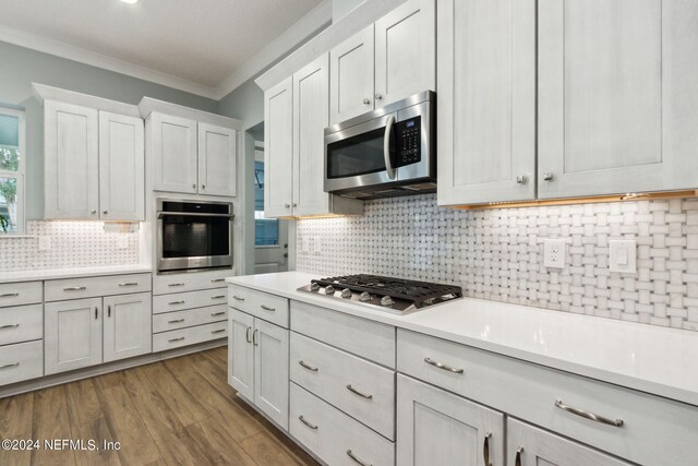 kitchen featuring stainless steel appliances, light countertops, crown molding, and tasteful backsplash