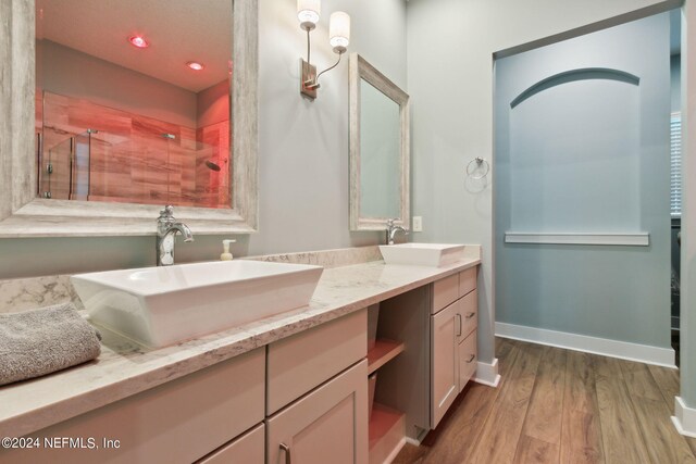 full bathroom featuring wood finished floors, double vanity, tiled shower, and a sink